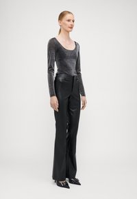 Schwarze Kunstleder-Hosen mit weitem Bein, kombiniert mit einem schimmernden silbernen Langarmtop mit Rundhalsausschnitt und figurbetonter Silhouette.