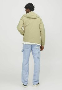 Lys khaki vandtæt jakke med hætte, parret med lyseblå cargo jeans med sidelommer. Glat tekstur, afslappet design.