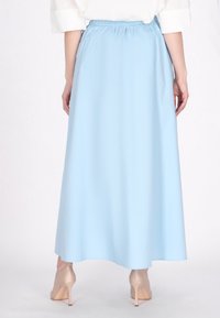 Jupe maxi bleu clair avec une taille élastique, présentant une texture lisse et un design plein et fluide. Portée avec des chaussures à talons beiges.
