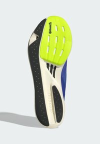 Suela de zapatilla con una base negra, acentos de goma verde brillante y un diseño perforado para una mejor tracción. Media suela blanca con detalle de la marca.