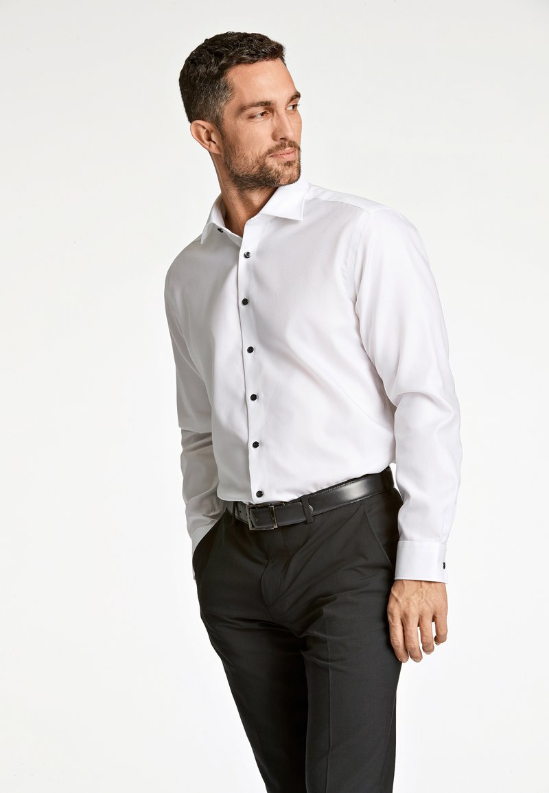 Wit overhemd met een puntkraag, slim fit ontwerp, zwarte knopen en lange mouwen, gecombineerd met zwarte broeken en een riem.