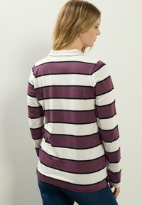 Langärmliges Polo-Shirt mit horizontalen Streifen in Lila- und Weißtönen sowie schwarzen Akzenten. Weicher Stoff mit entspanntem Schnitt.