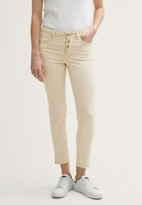 Beige denim jeans met een slim fit, vijf zakken en een knoopsluiting. Draagt met witte sneakers en een aansluitend wit topje.