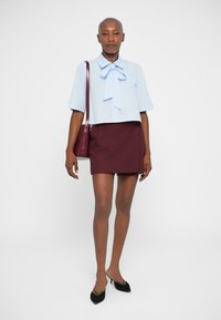 Lichtblauwe cropped blouse met strik, korte mouwen, gecombineerd met een bordeaux mini-jurk. Zwarte puntige hakken en een kleine bordeaux handtas.