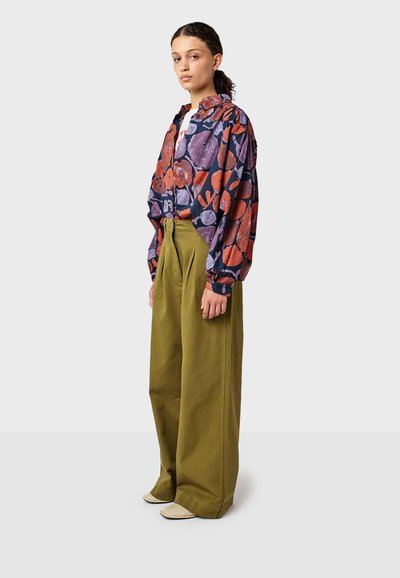 Farebná kvetinová blúzka s červenými, fialovými a námorníckymi vzormi, doplnená vysokými olivovo zelenými širokými nohavicami a krémovými topánkami.