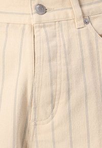 Light beige trousers with vertical blue stripes, featuring a front pocket, metal button closure, and woven texture.