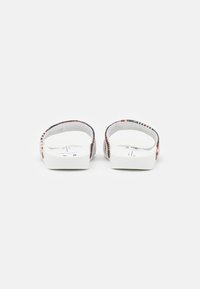 Λευκές σανδάλια με υφασμάτινες, ανάγλυφες λωρίδες σε κόκκινο, μαύρο και γκρι. Σχεδίαση με ανοιχτή πλάτη, επίπεδη σόλα και μινιμαλιστική λεπτομέρεια.