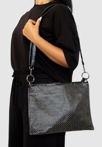 Bolso negro con un acabado brillante, adornado con tachuelas plateadas, con una correa desmontable y cierre de cremallera, de forma rectangular.