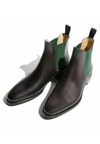 Botas Chelsea de cuero marrón con paneles elásticos verdes en los laterales y suelas negras, con un acabado suave y un diseño de punta afilada.