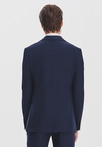 Granatowa marynarka widziana z tyłu, o dopasowanym kroju, gładkiej fakturze materiału i subtelnym wzmocnieniu ramion.