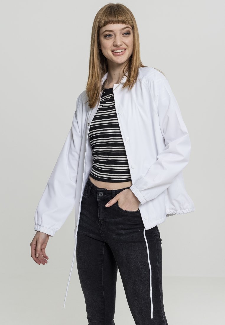 Jachetă albă tip windbreaker, cu manșete elastice și tiv cu șnur, purtată peste un top scurt cu dungi alb-negru și blugi negri.