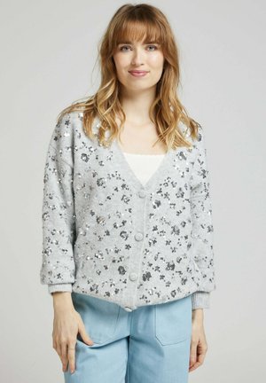 Gilet en tricot gris avec des sequins argentés, doté d'un col en V, d'une fermeture à boutons et de poignets côtelés. Coupe décontractée avec des embellissements floraux.