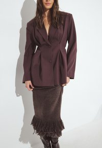 Bordový strihaný blejzer s veľkými klopami a dvomi gombíkmi, spárovaný s textúrovanou hnedou sukňou s třásňovým lemom.