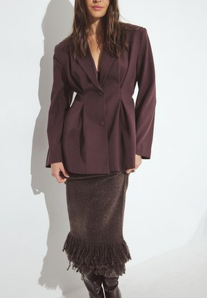 Bordeaux op maat gemaakte blazer met grote revers en twee knopen, gecombineerd met een gestructureerde bruine rok met een franjeszoom.