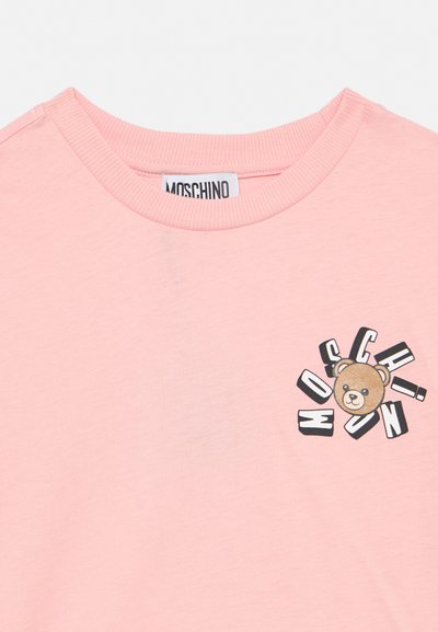 Ροζ ανοιχτό ροζ μπλουζάκι με στρογγυλή λαιμόκοψη, ετικέτα Moschino στο εσωτερικό γιακά και γραφικό αρκουδάκι περιβαλλόμενο από το κείμενο "Moschino" στο στήθος.