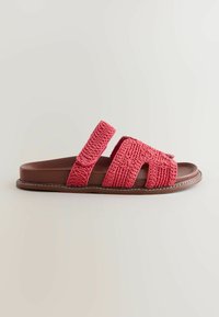 Sandale marron avec deux brides en crochet rose texturé, une sur les orteils et une autour de la cheville, sur un fond clair.