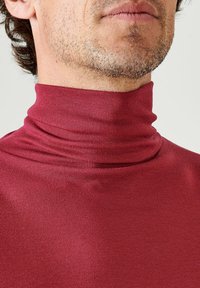 Maglione a collo alto rosso a coste con un collo aderente, texture liscia e un leggero lucido. Il materiale si estende per offrire comfort.