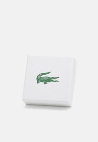Cutie albă rectangulară cu suprafață texturată, având un logo verde de crocodil pe partea din față. Design simplu și curat.