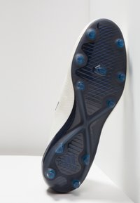 Botín de fútbol blanco con un upper texturizado, acentos azules y suela negra con tacos. Presenta un logo de Adidas y un diseño aerodinámico.