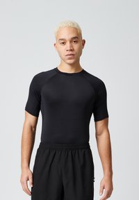 Zwarte sportieve T-shirt met korte mouwen, gemaakt van rekbare stof, met een ronde hals en een strakke pasvorm, gecombineerd met losse zwarte shorts.