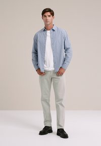 Hellblau-weiße karierte Button-Down-Bluse über einem weißen T-Shirt, kombiniert mit hellgrauen Hosen und schwarzen Schuhen. Einfaches und lässiges Design.