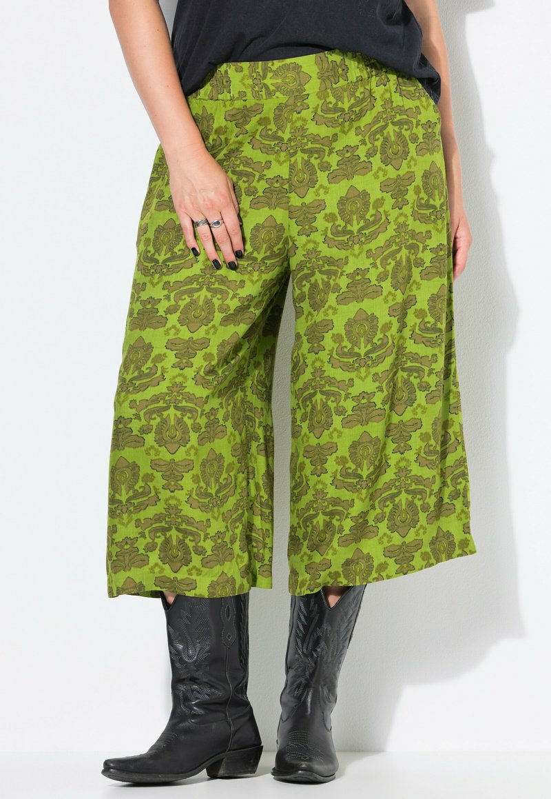 Groene culottes met een bloemenpatroon, featuring een elastische tailleband en wijde pijpen, gecombineerd met zwarte cowboylaarzen.