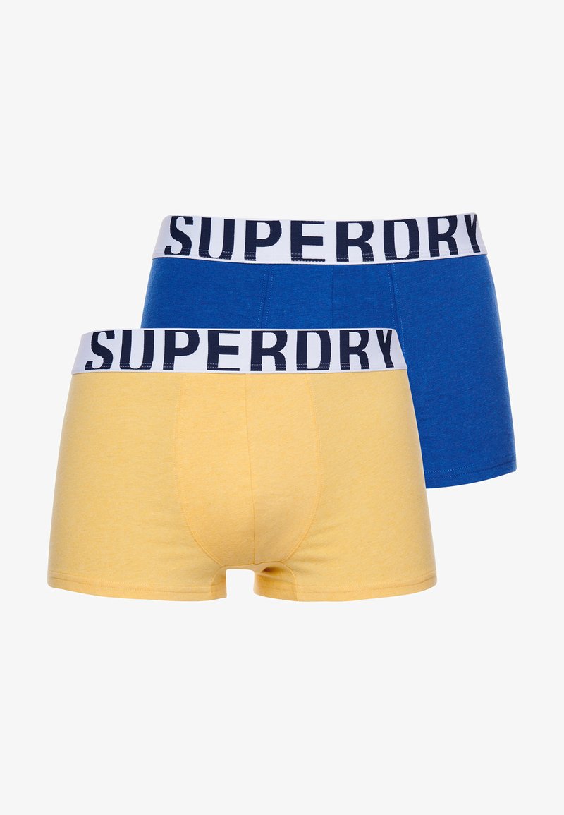 Twee paren heren boxer shorts: één in het blauw en één in het geel, beide met een witte band met "SUPERDRY" in marineblauw erop gedrukt.