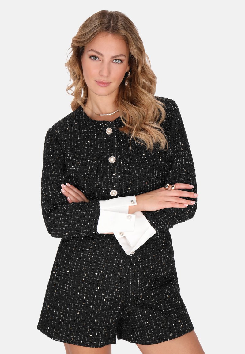 Romper negro de textura, de manga corta con detalles en plateado, que presenta botones de perla y puños blancos. Diseño clásico con un ajuste estructurado.