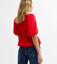 Blouse rouge à manches courtes avec une finition texturée, taille cintrée avec un lien, et coupe décontractée. Associée à un jean en denim bleu taille haute.
