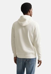 Sweat à capuche blanc à texture douce avec capuche à cordon, vu de dos, associé à un jean bleu. Design simple et décontracté.