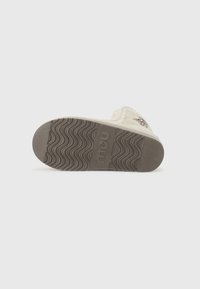 Lys beige tøffel med en tekstureret gummisål, der har et flettet design på overdelen og et præget logo på ydersålen.
