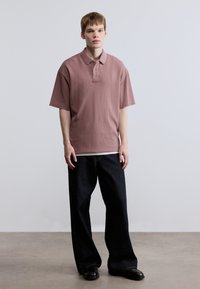 Πόλο μπλούζα με κοντά μανίκια και χαλαρή εφαρμογή σε ανοιχτό μωβ χρώμα, υφασμένη με υφή, με γιακά και διακριτικό λογότυπο. Συνδυασμένη με σκούρα, φαρδιά τζιν.