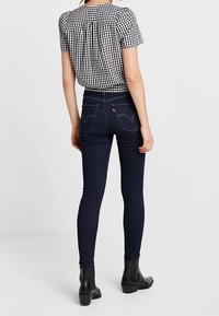 Camisa de cuadros en blanco y negro de manga corta con espalda fruncida, combinada con vaqueros skiny oscuros y botas negras de tobillo. Diseño minimalista.