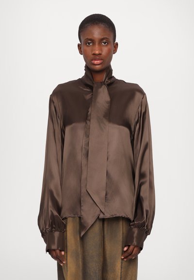 Blouse longue en satin marron à manches longues, avec un col haut et un devant noué, présentant des manches bouffantes et des poignets froncés. Texture lisse avec un subtil éclat.