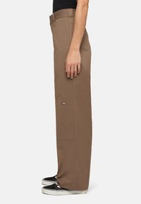 Bruine straight-leg broek van een textuurstof, met zijzakken en een geborduurd logo op de linker bovenbeen. Gemaakt om te dragen met zwarte sneakers.