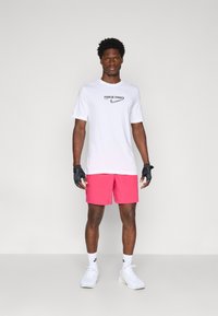 White short-sleeve Nike Pro shirt with logo, paired with bright pink shorts. Black gloves and white sneakers complete the athletic look.
