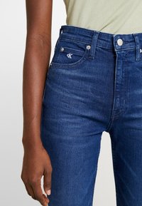 Högmidjade mörkblå jeans i denim, med CK-logotyp på framfickan, silverdetaljer och en figurnära design.