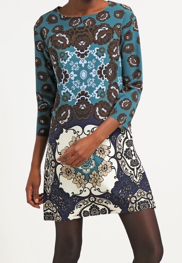 Långärmad klänning med ett tealfärgat, brunt och krämfärgat blommönster och kontrasterande paneler. Tyget framstår som slätt med en figursydd silhuett.