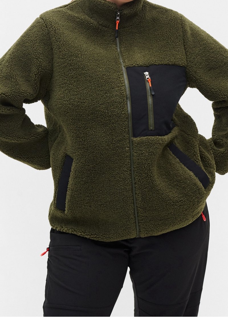 Giacca in pile verde oliva con colletto alto, tasca sul petto con zip e dettagli neri. Presenta zip arancioni e tasche laterali.