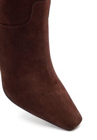 Stivaletti in suede marrone con punta affusolata e superficie liscia. Presentano un sottile contorno cucito vicino al bordo superiore.