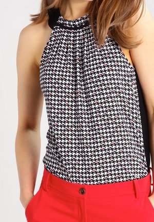 Mujer que lleva un top sin mangas con estampado de pata de gallo en blanco y negro, combinado con pantalones de talle alto en rojo brillante con bolsillos delanteros.