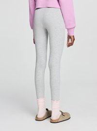 Leggings grigie con una texture liscia e un design aderente, abbinate a calzini rosa chiaro con volant e scarpe slip-on marroni.