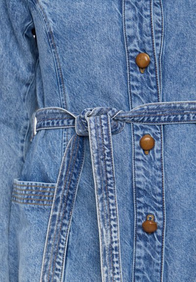 Lys blå denimjakke med belte i livet, med solid knappelukking, teksturert stoff og en sidelomme med sømdetaljer.