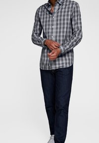 Szara i biała koszula w kratkę z długimi rękawami, połączona z ciemnoniebieskimi dżinsami i białymi trampkami. Widoczna gładka faktura materiału.