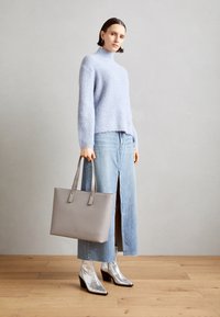 Suéter de punto azul claro, falda de mezclilla con abertura frontal, bolso gris con asas dobles y botines plateados con tacones cuadrados.