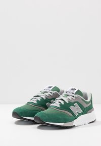 Zelené a šedé tenisky s svrchním materiálem z semiše a síťoviny, kulatou špičkou, texturovanou podrážkou a reflexními detaily po stranách.