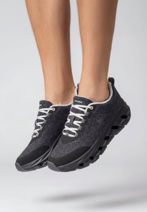 Legs wearing dark gray sneakers with white laces and thick black soles, shown mid-air against a plain light background.