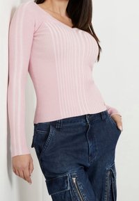 Světle růžový žebrovaný top s dlouhým rukávem a výstřihem do V, doplněný tmavě modrými cargo kalhotami s bočními kapsami na zip.