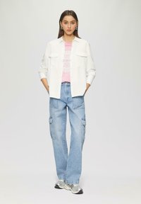 Weißes Hemd, pinkes Grafik-T-Shirt, hellblaue Cargo-Jeans und silberne Sportschuhe. Das Outfit hat einen lockeren Schnitt.