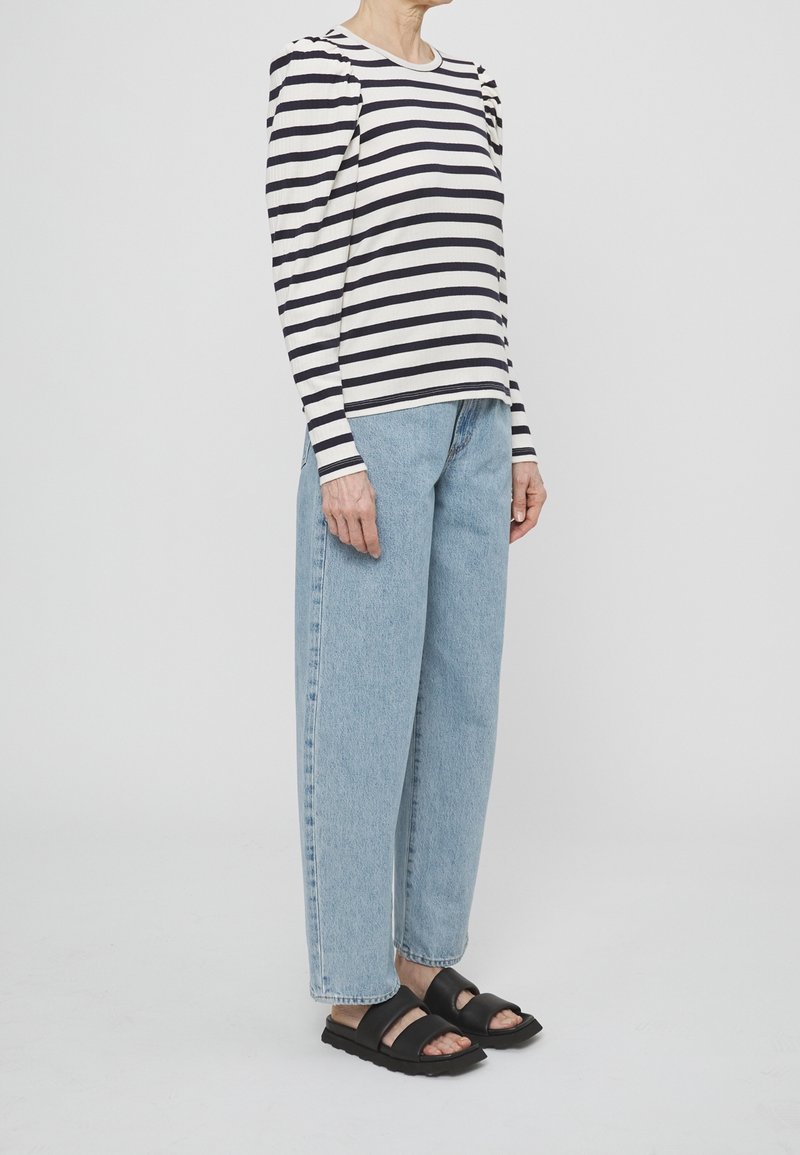 Haut à manches longues rayé bleu marine et crème, avec épaules bouffantes, associé à un jean large bleu clair et des sandales noires à enfiler.